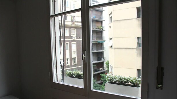 Una finestra che si affaccia su un edificio con balconi e un piccolo giardino.