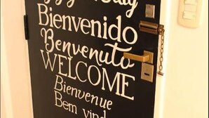 Una porta con un cartello di benvenuto in diverse lingue, un lucchetto e una serratura.