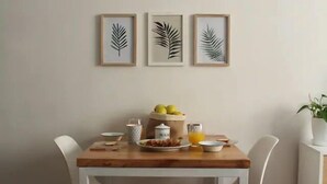 Zona pranzo con tavolo in legno, sedie bianche e un'opera d'arte a tema foglie appesa al muro.