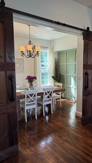 A dining area with a wooden table and chairs, a chandelier, and a window with curtains.