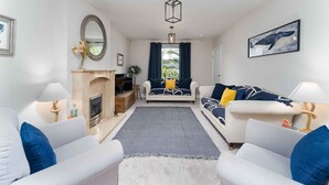 Un salon avec une cheminée, deux canapés, un tapis et une grande fenêtre avec des rideaux.