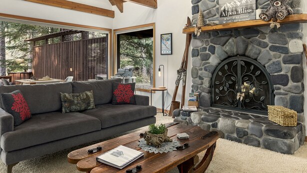Un salon chaleureux avec une cheminée en pierre, des poutres apparentes en bois au plafond, un canapé gris et une table basse en bois.