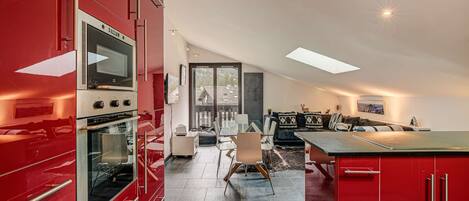 Una cocina moderna con armarios rojos, un comedor con mesa de vidrio y vistas al exterior.