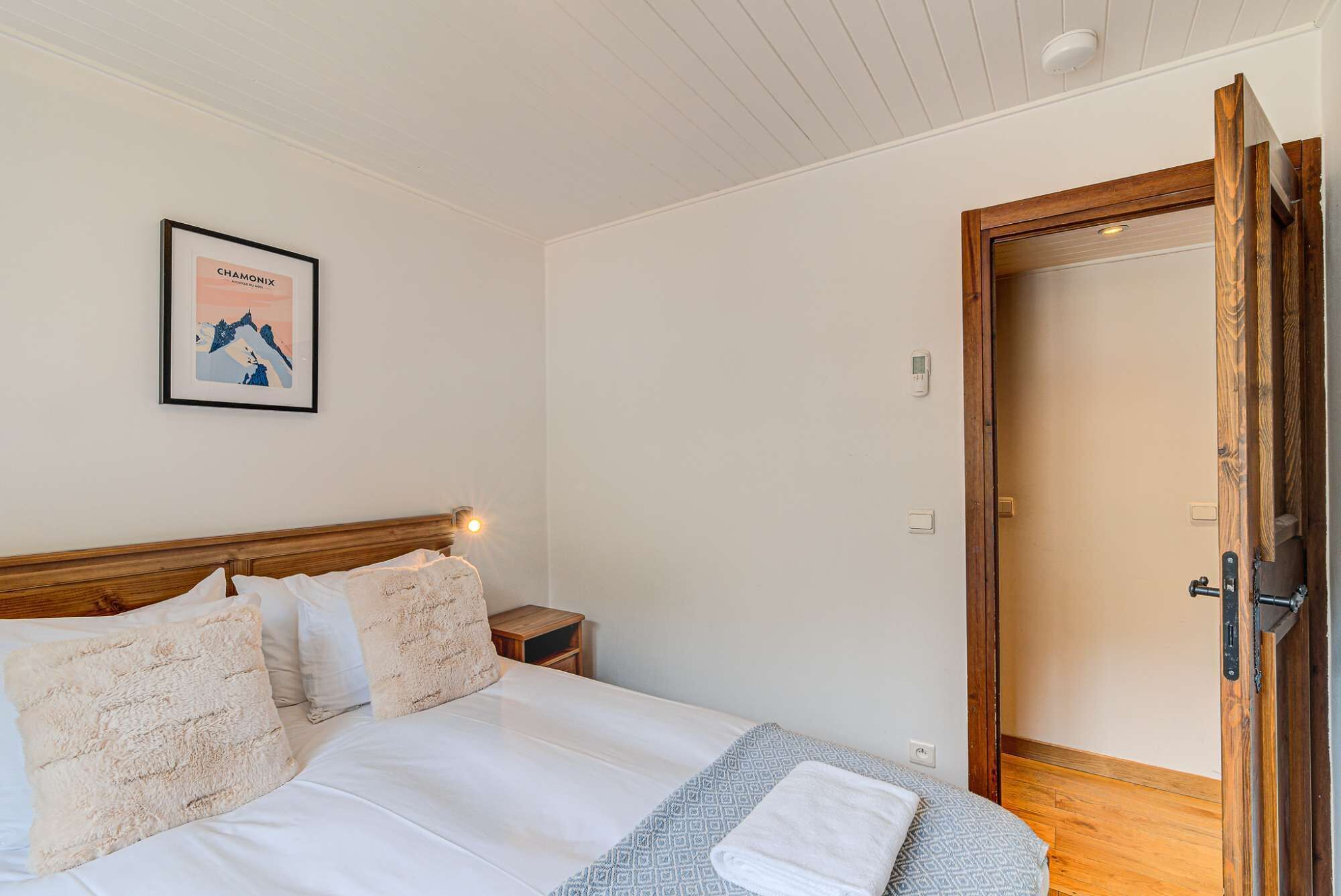 Une chambre à coucher avec une tête de lit en bois, un lit recouvert de draps blancs, une table de chevet avec une lampe et une porte dotée d’un cadre en bois.