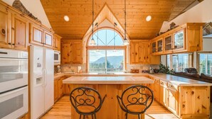 Een keuken met houten kasten, een groot eiland met twee stoelen en uitzicht op het buitengebeuren door een raam.