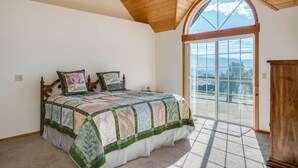 Een slaapkamer met een groot bed, een houten plafond en uitzicht door een glazen deur.