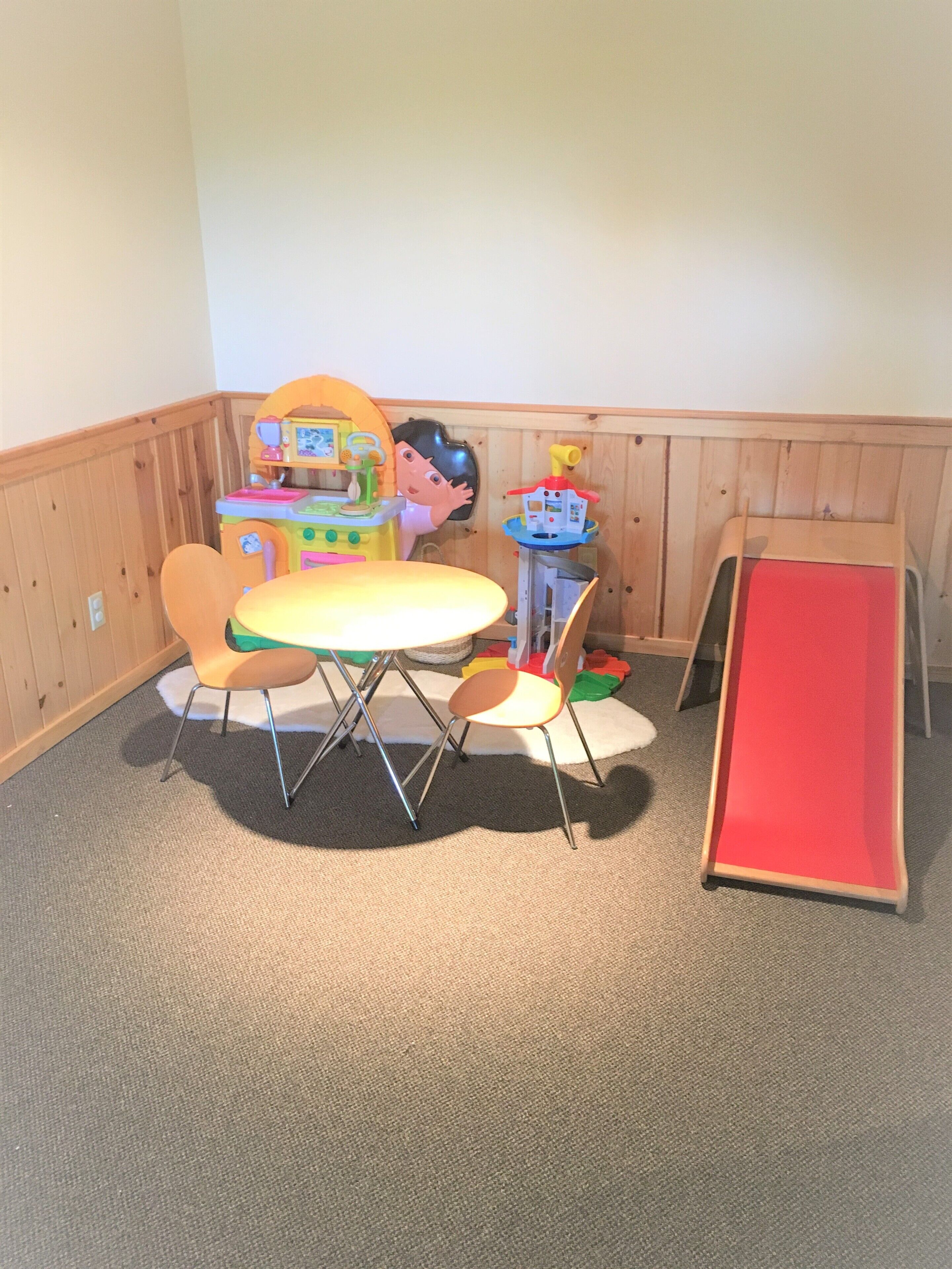A playroom with a table, chairs, a toy kitchen set, and a slide.