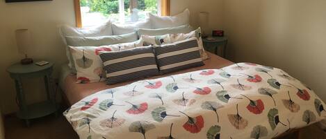 Quarto com cama, almofadas, mesa de cabeceira, abajur e quadros na parede.