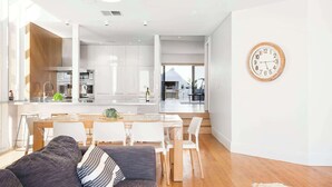 A modern kitchen with white cabinets and a dining area with a wooden table and white chairs. - Spectacular Panoramic Oceanview House in Seacliff (Seacliff)