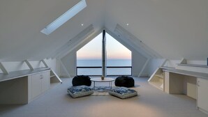 A room with a sloped ceiling, a view of the sea, and a seating area with cushions. - Spectacular Panoramic Oceanview House in Seacliff (Seacliff)