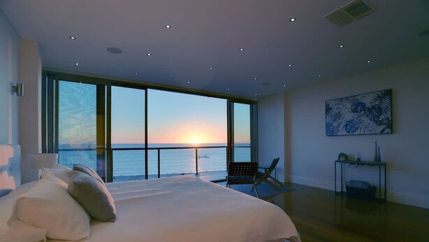A bedroom with a large bed, a chair, a small table, and a painting. - Spectacular Panoramic Oceanview House in Seacliff (Seacliff)