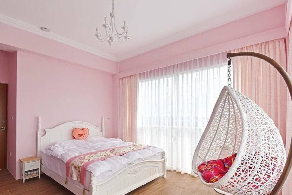 Un dormitorio con cama, mesita de noche, sillón colgante y puerta de madera.