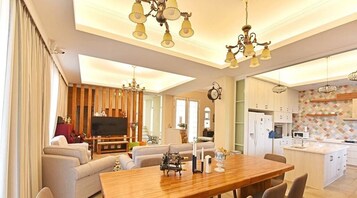 Una sala moderna con una mesa de comedor de madera, sofás y un televisor. La cocina cuenta con armarios blancos y un salpicadero de azulejos.