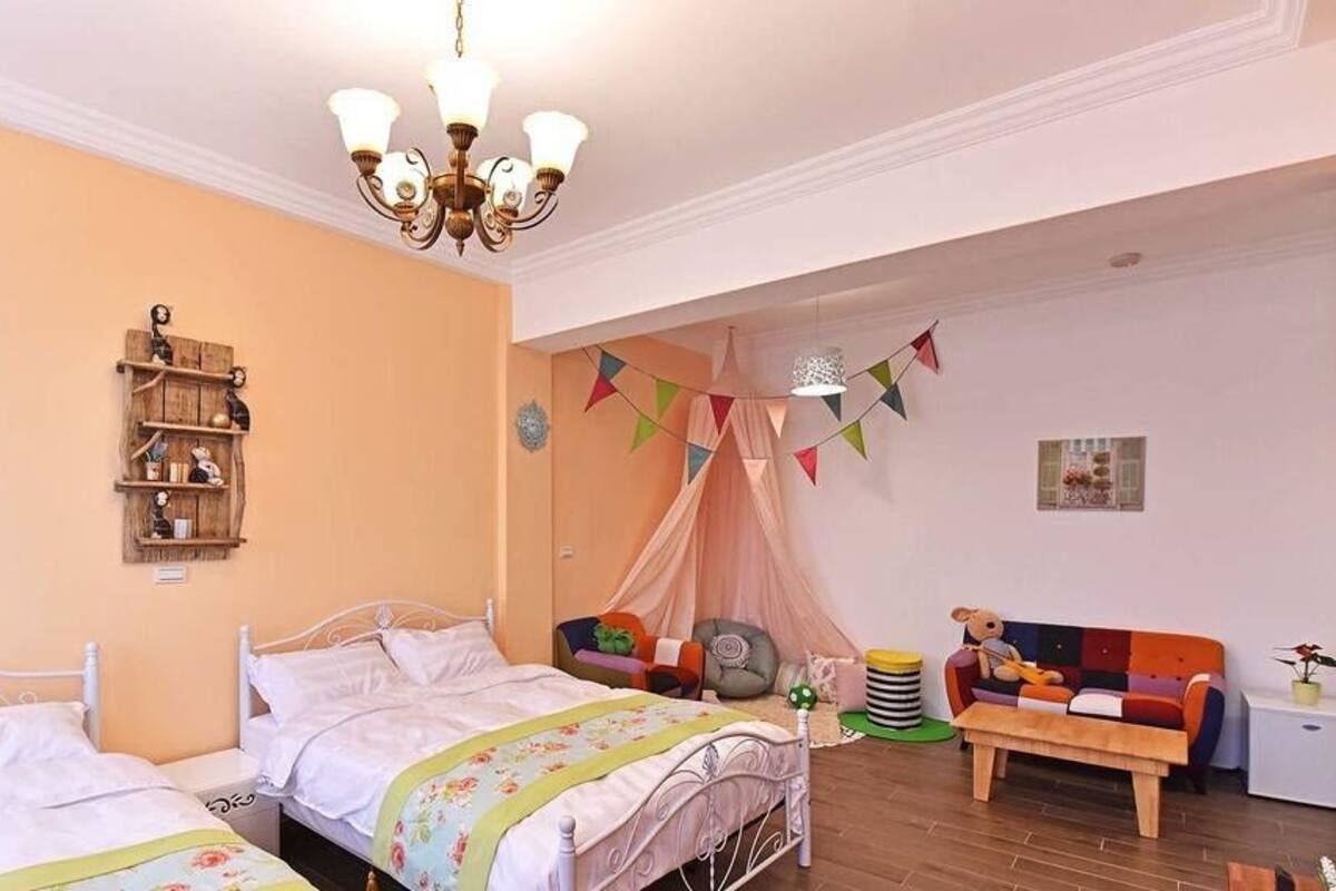 Un dormitorio con dos camas, una estantería de madera, un sofá colorido y una mesita pequeña.