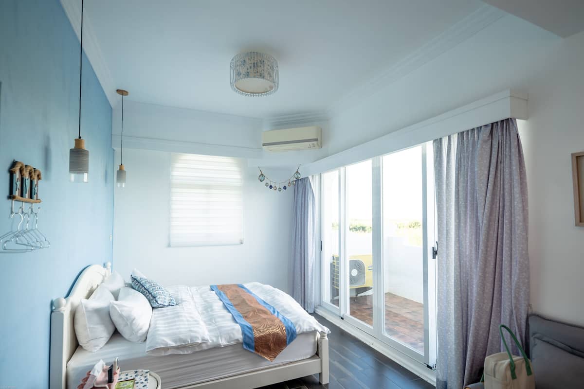 Un dormitorio con cama, ventana y puerta corredera de vidrio que da a un espacio al aire libre.