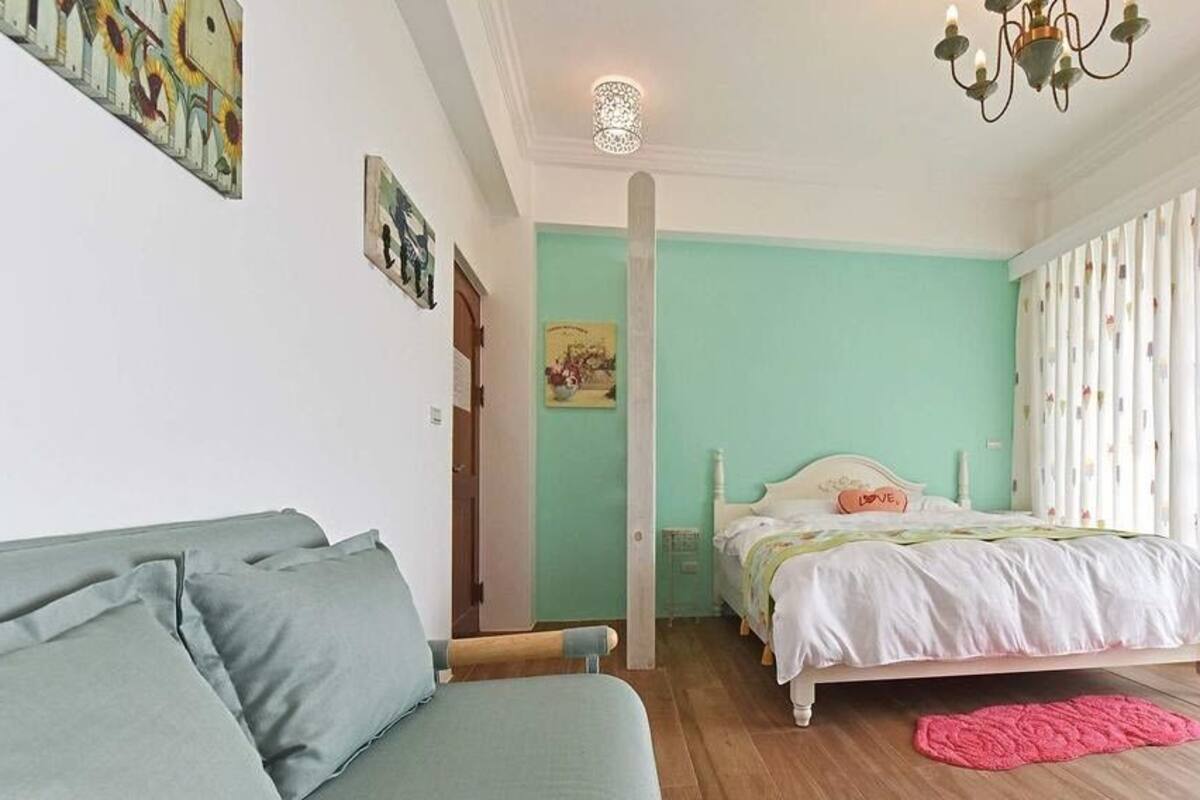 Un dormitorio con cama, sofá, ventana con cortinas y obras de arte en las paredes.