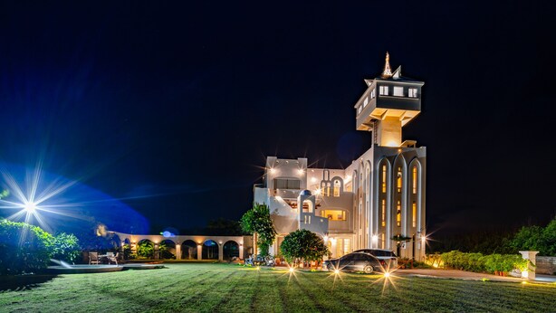 Um edifício moderno com uma torre imponente e janelas em arco, cercado por um gramado bem iluminado e um carro estacionado.