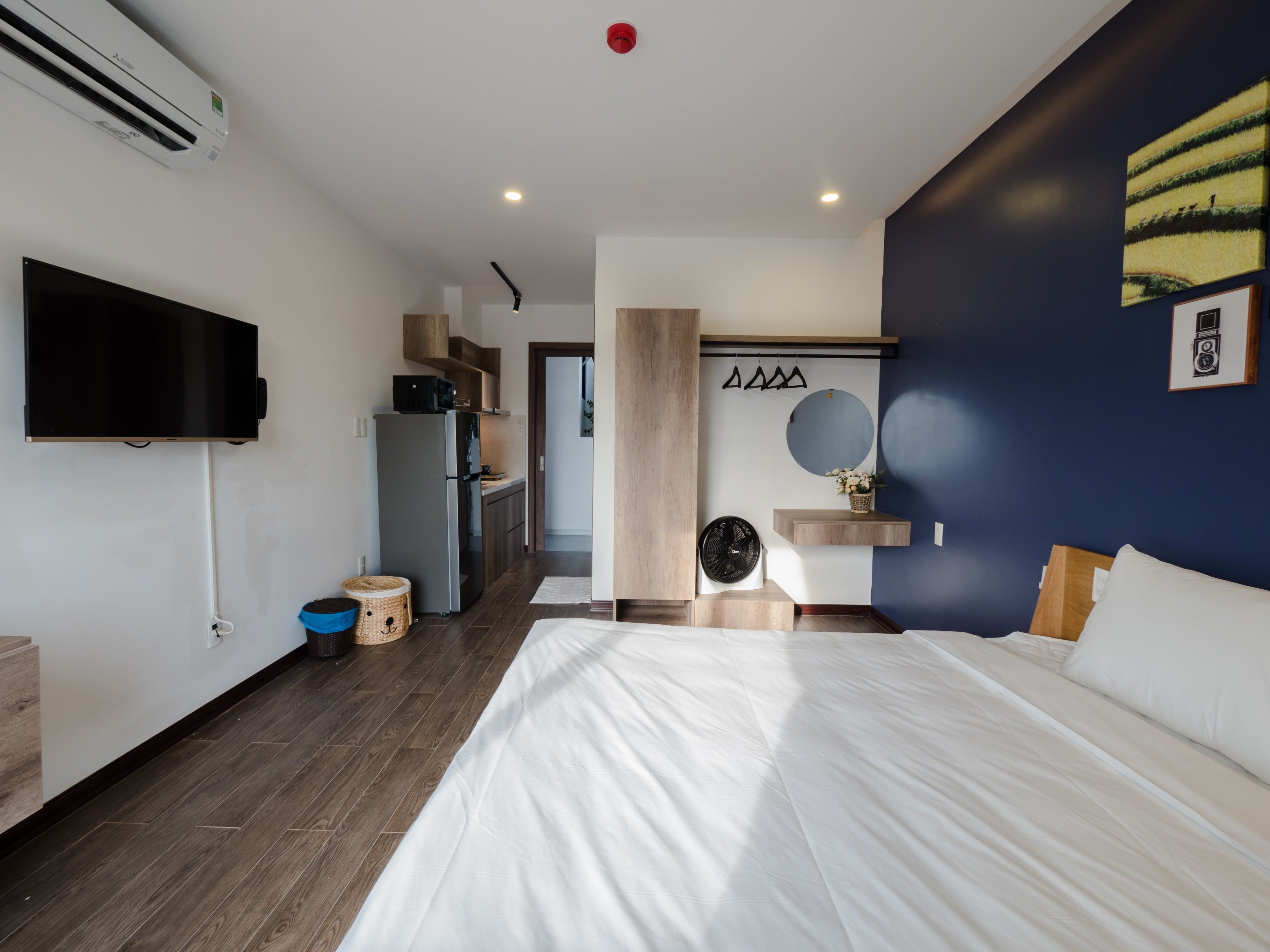 A modern hotel room with a bed, a TV, a kitchenette, and a bathroom.