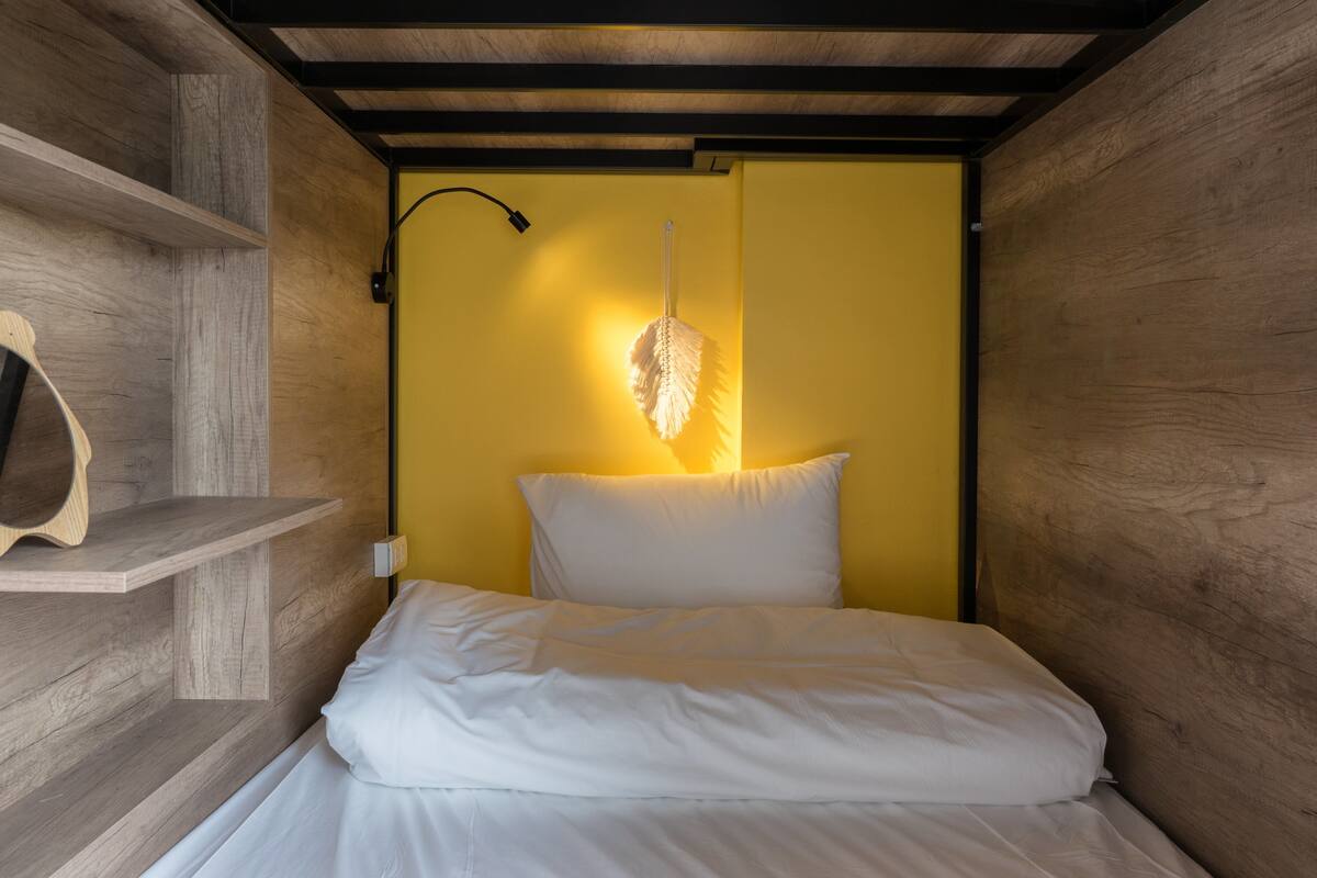 A bed in a room with wooden walls and a yellow accent wall.