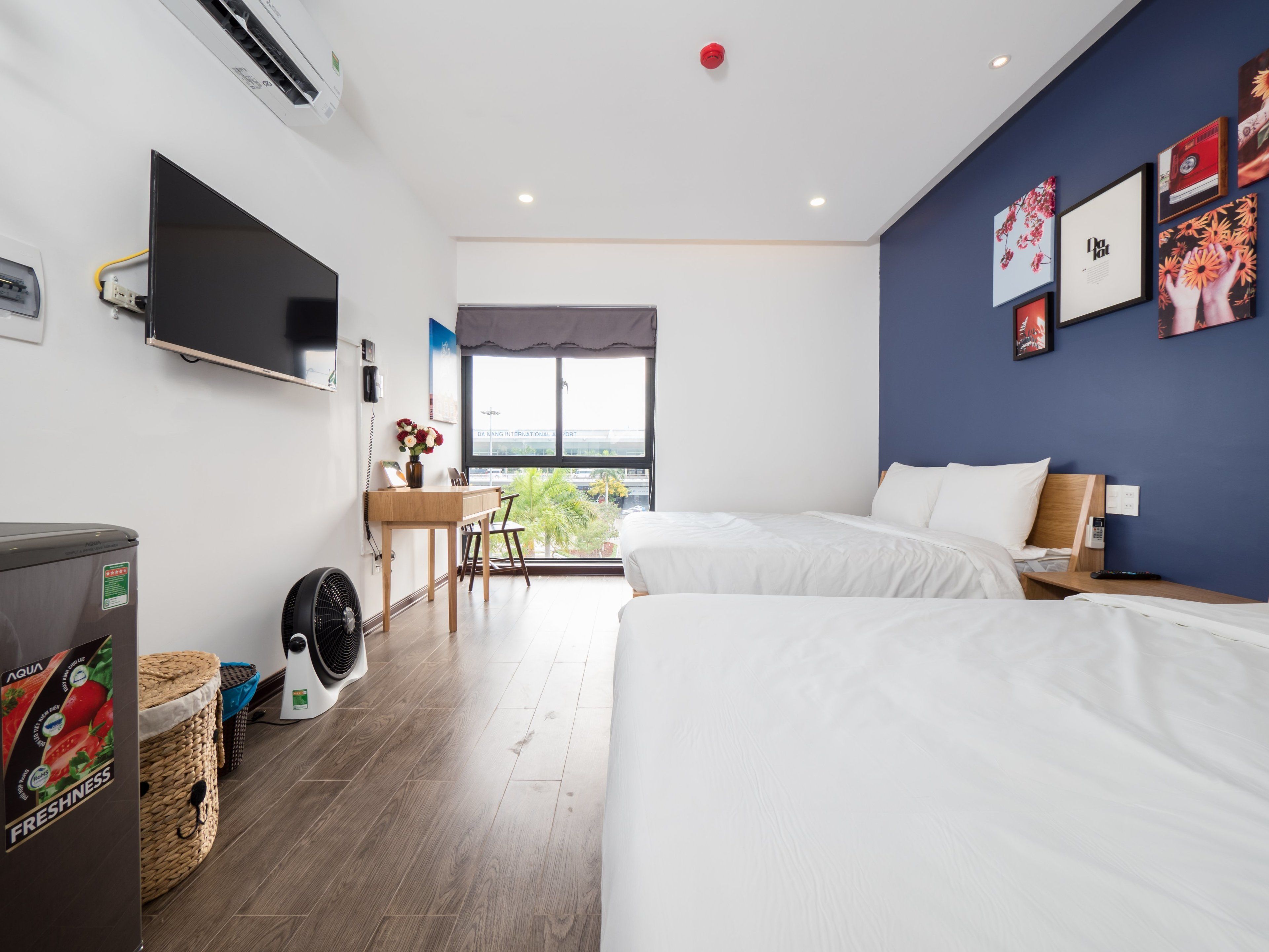 Habitación de hotel con dos camas, un escritorio con silla, televisor montado en la pared y ventana con vistas a la ciudad.