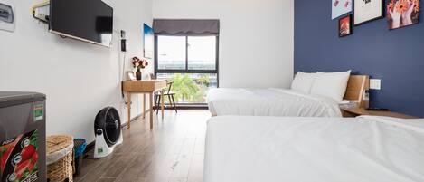 Habitación de hotel con dos camas, un escritorio con silla, televisor montado en la pared y ventana con vistas a la ciudad.