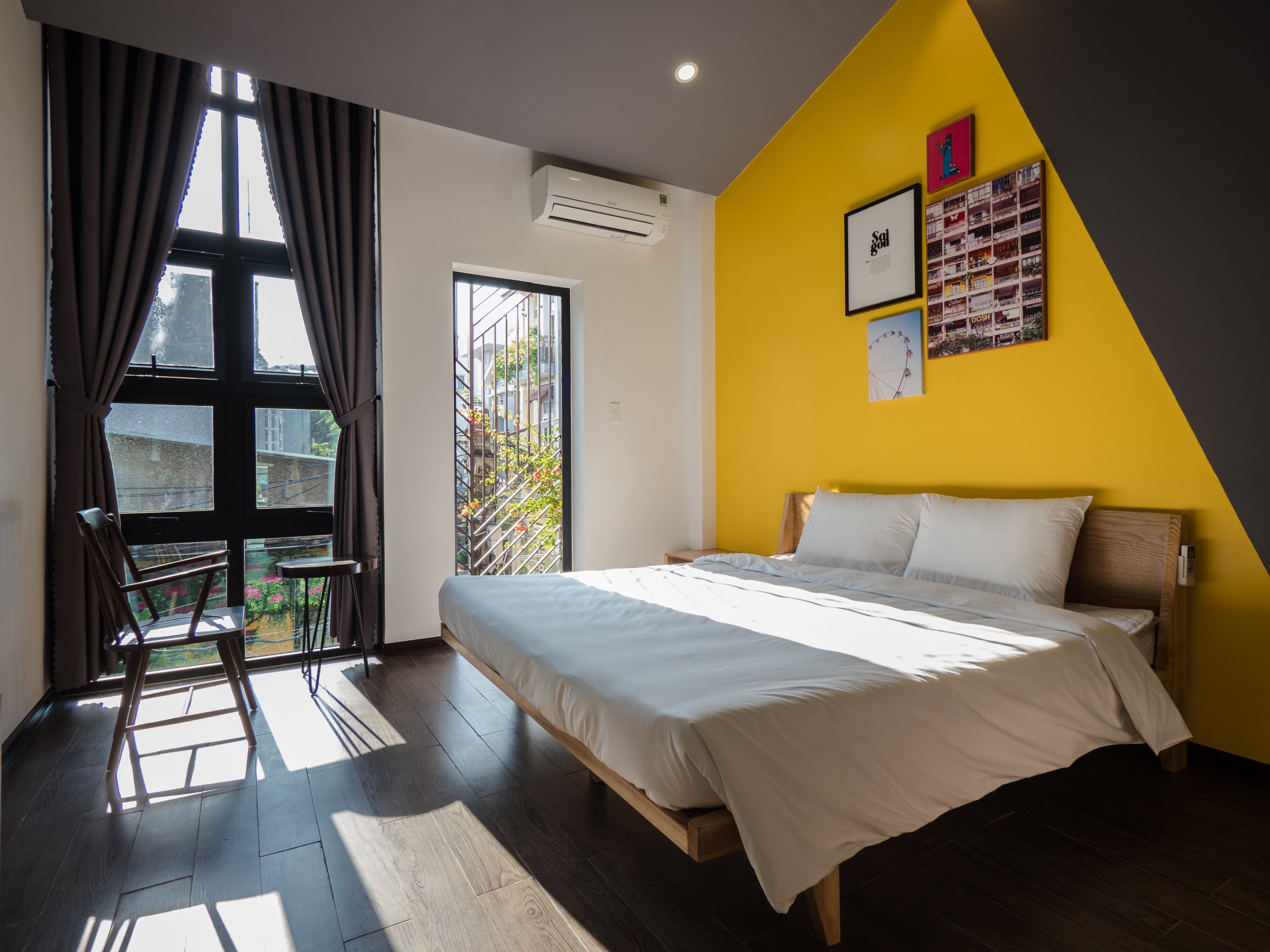 A bedroom with a bed, a window with curtains, a ladder, and a wall with framed pictures.