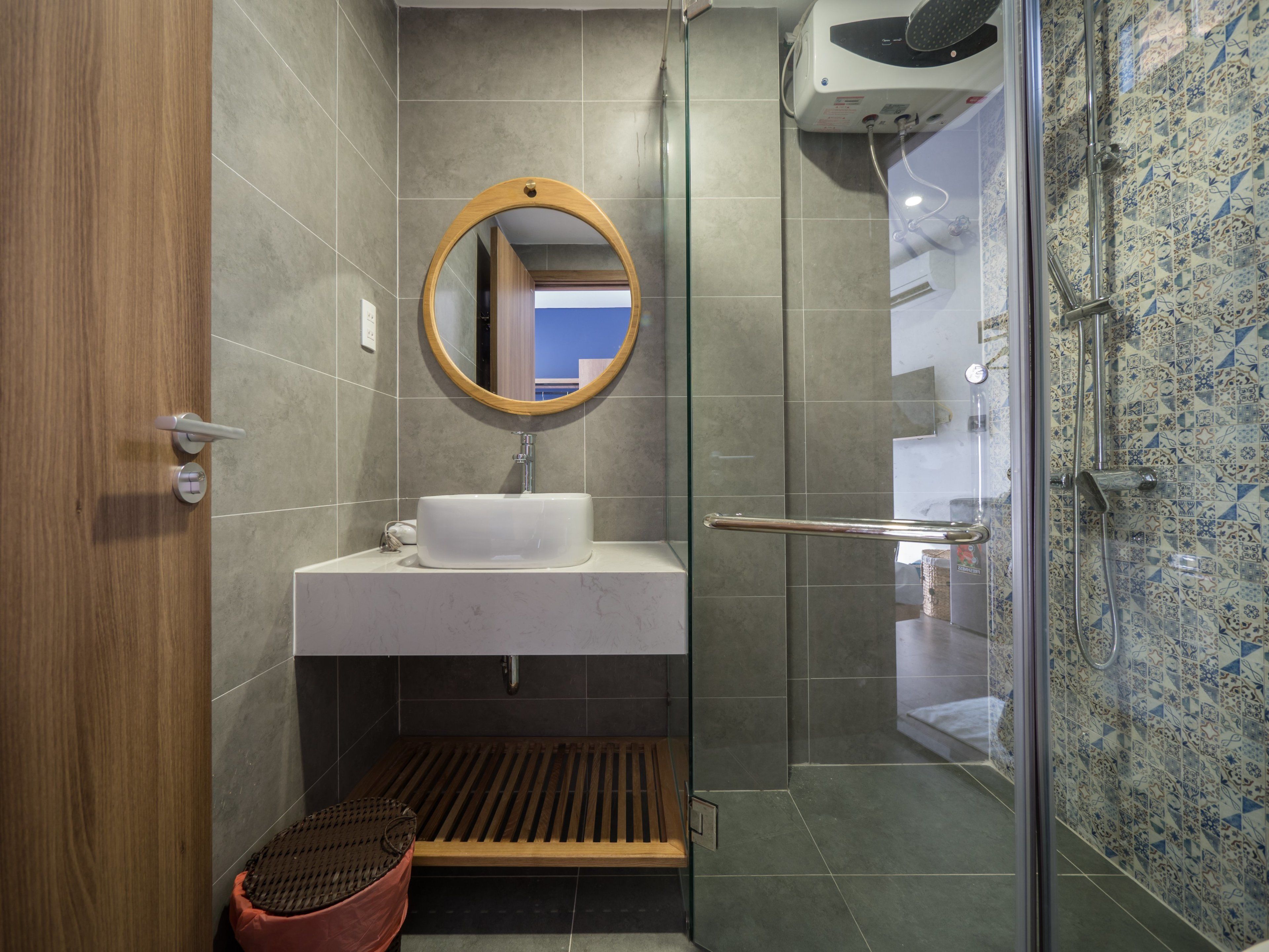 Une salle de bain avec un lavabo blanc, un miroir encadré en bois et un espace douche doté d’une porte en verre.