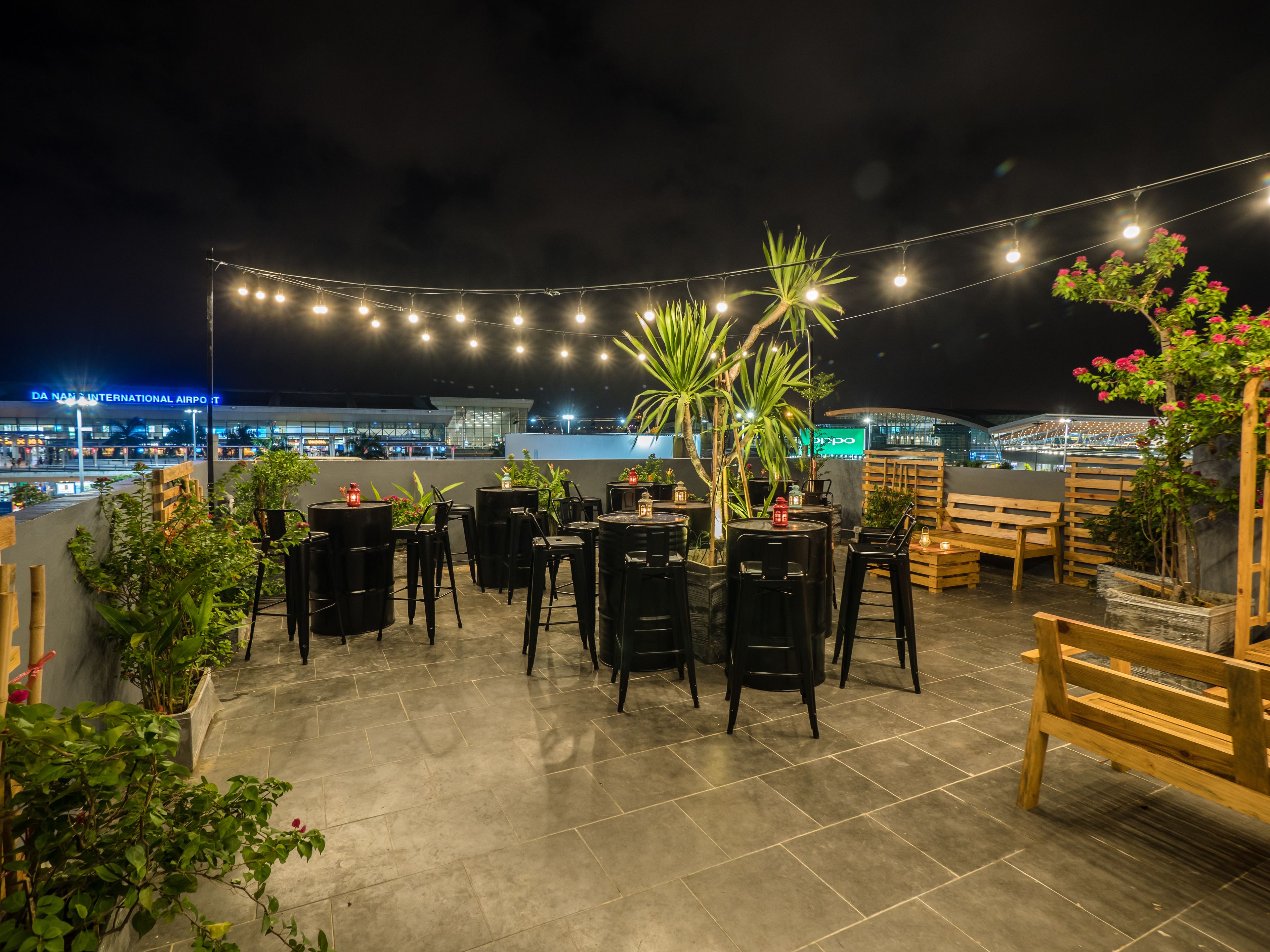 An outdoor seating area with tables and chairs, string lights, and potted plants.