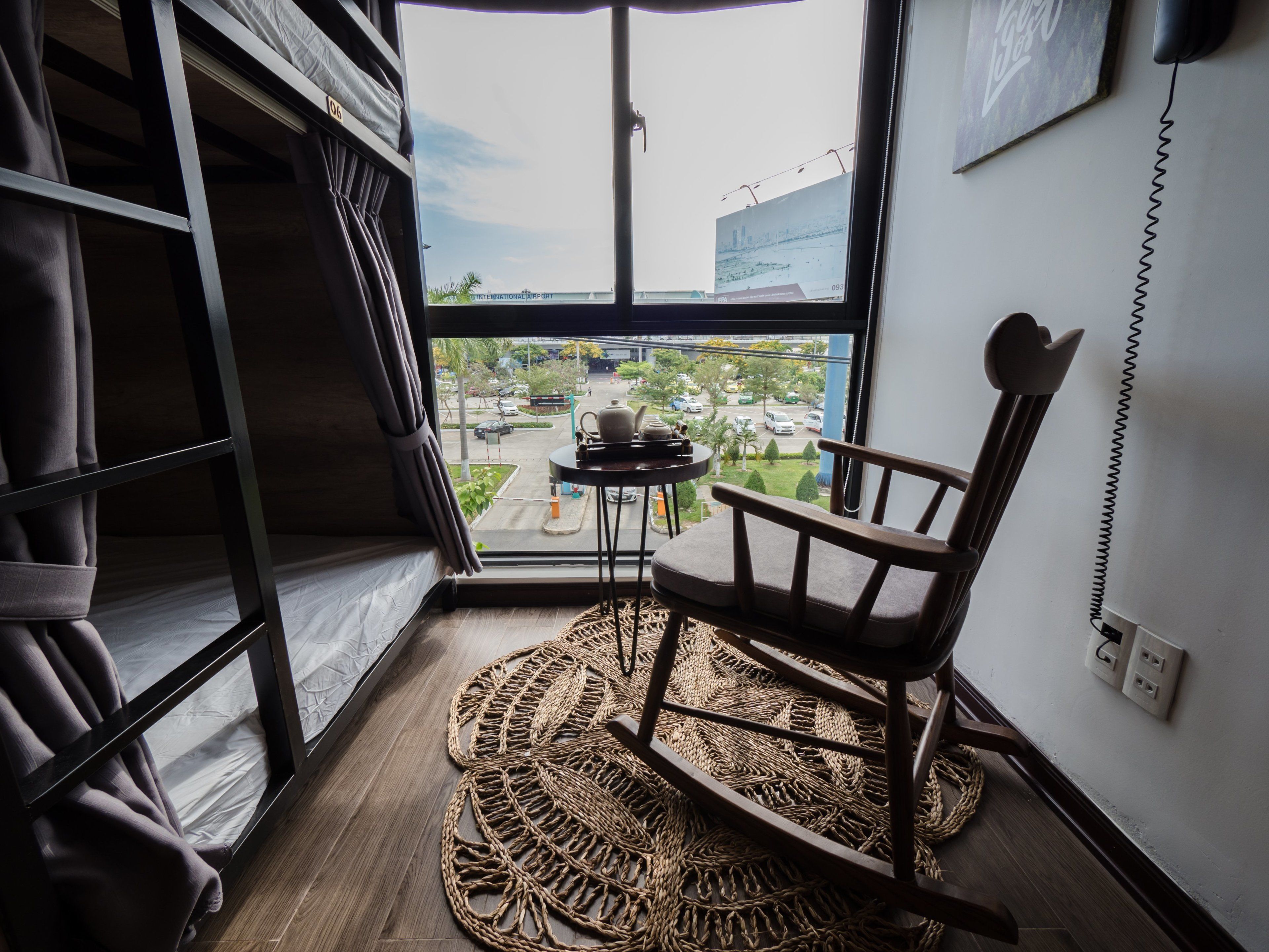 A room with a large window, a chair, a small table, and a woven mat on the floor.