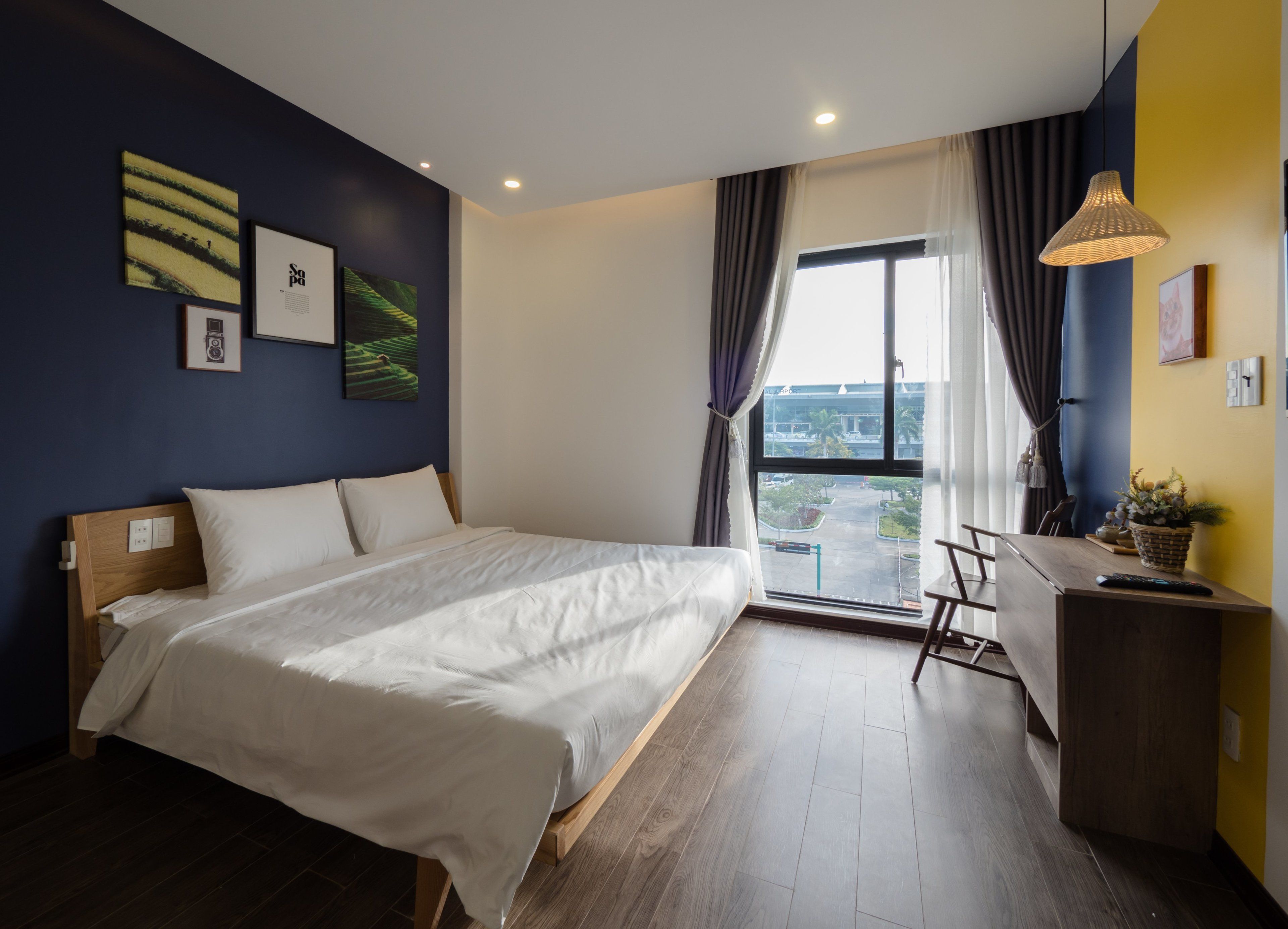 A modern hotel room with a large bed, a desk, and a view of the cityscape through the window.