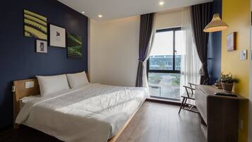 A modern hotel room with a large bed, a desk, and a view of the cityscape through the window.