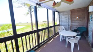 A covered porch with a table and chairs, overlooking a grassy area with a body of water.
