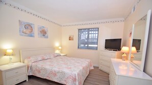 A bedroom with a bed, nightstands, a dresser, a television, and a window with blinds.