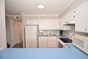 Une cuisine de taille réduite avec des meubles blancs, un lave-vaisselle, une cuisinière et un four à micro-ondes.