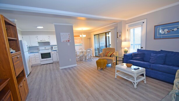 A modern living room with a blue sofa, a wicker coffee table, and a dining area with white chairs.