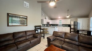 A spacious living room with two brown leather sofas, a wooden coffee table, and a ceiling fan.