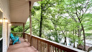 A wooden deck with a railing, two blue chairs, and a view of trees.