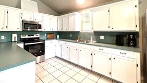 A kitchen with white cabinets, a microwave, an oven, a sink, and a coffee maker.