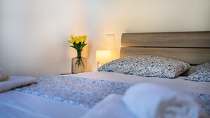 Cama bem arrumada com roupa de cama floral, uma luminária de cabeceira e um vaso de flores amarelas.
