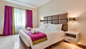 Habitación de hotel con una cama grande, una mesita de noche con lámpara y una ventana con cortinas.