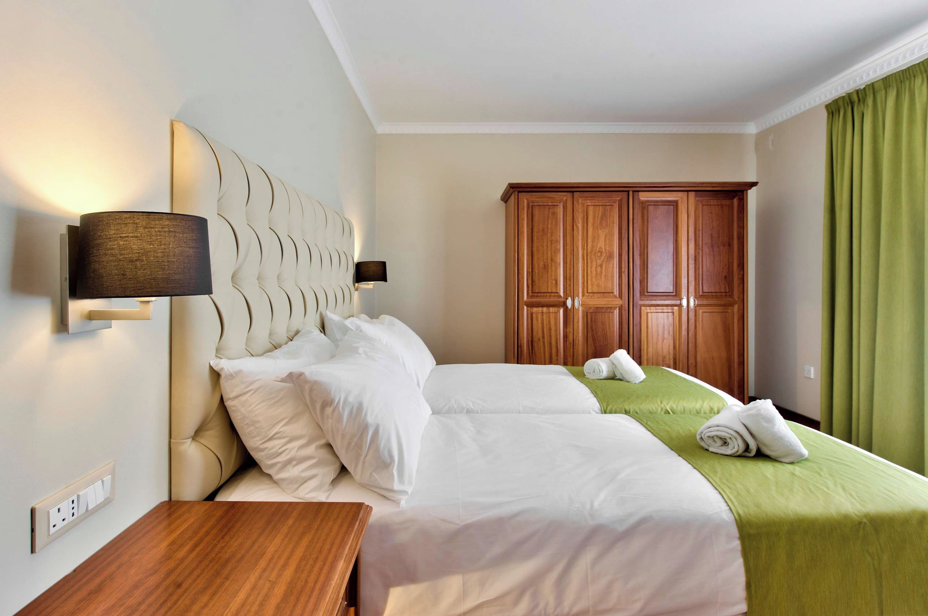 A hotel room with a large bed, a nightstand, a wooden wardrobe, and a green curtain.