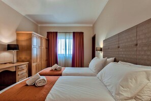 A hotel room with two beds, a wooden wardrobe, a desk with a lamp, and a window with curtains. - Villa Stephanotis~ Villa w/ Private Pool & Views (Il-Mellieħa)