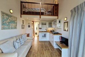A cozy interior with a sofa, a kitchen area, and a staircase leading to an upper level. - Steepfield Studio, bijou apartment Bantham S.Devon (Bantham, Kingsbridge)
