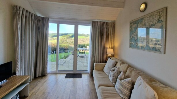 A living room with a sofa, a television, and a view of a landscape through a glass door. - Steepfield Studio, bijou apartment Bantham S.Devon (Bantham, Kingsbridge)