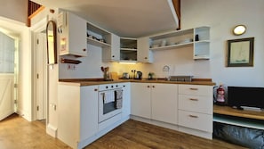 A compact kitchen with white cabinetry, a built-in oven, a sink, and a fire extinguisher. - Steepfield Studio, bijou apartment Bantham S.Devon (Bantham, Kingsbridge)