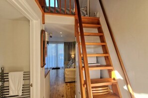 A wooden staircase leading to a living area with a sofa and a lamp. - Steepfield Studio, bijou apartment Bantham S.Devon (Bantham, Kingsbridge)
