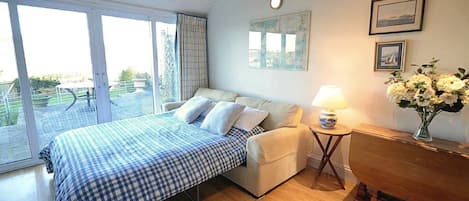 Un dormitorio con cama, mesita de noche, lámpara, un florero y vistas por la ventana.