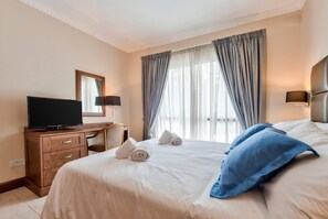 Une chambre d’hôtel avec un lit, un téléviseur posé sur une commode en bois, une lampe et une fenêtre avec des rideaux.