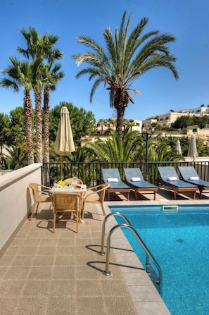 Un espace aménagé au bord de la piscine, avec des chaises longues, une table décorée de fleurs et des palmiers.
