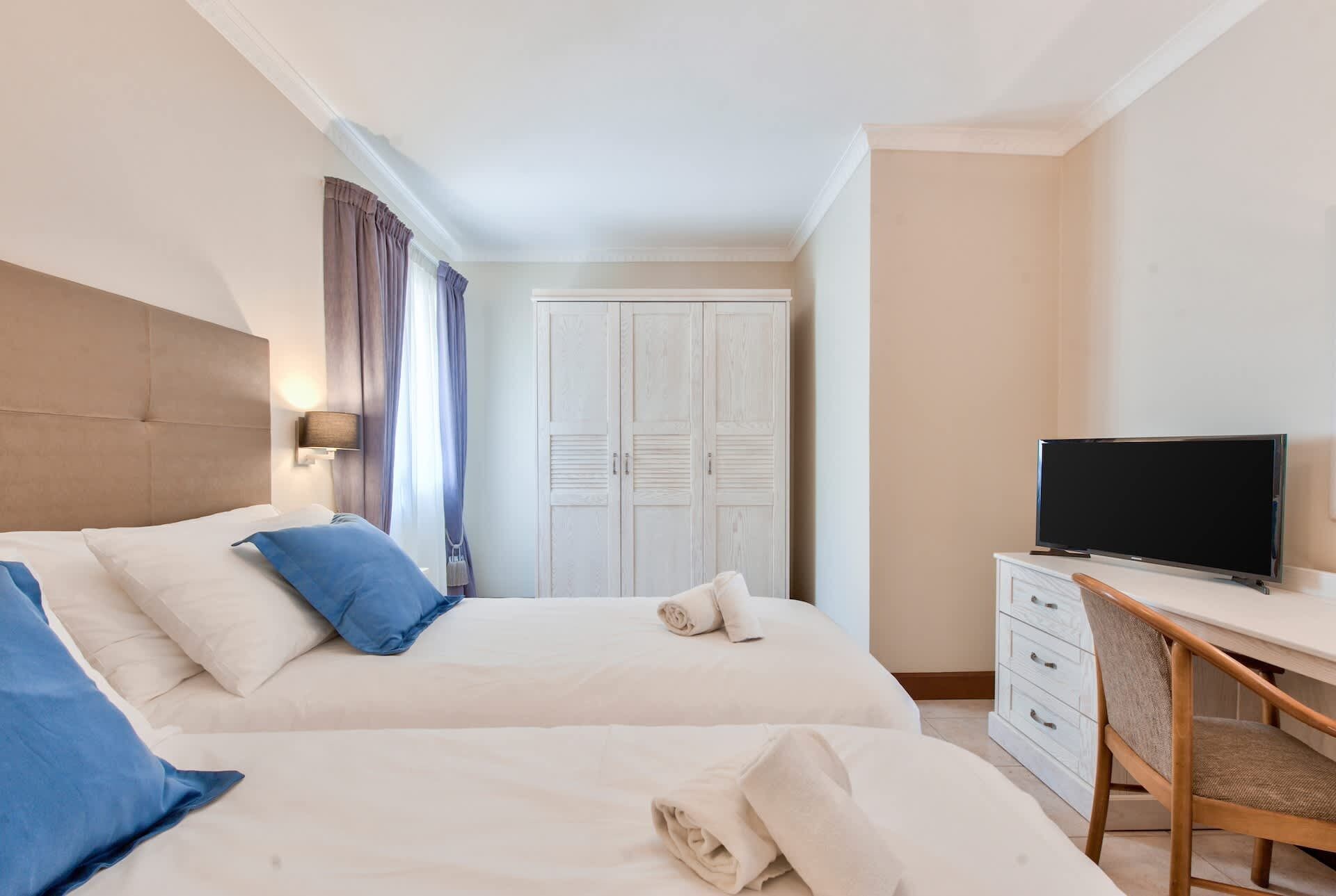 Une chambre d’hôtel avec deux lits, un bureau avec une télévision et une armoire.